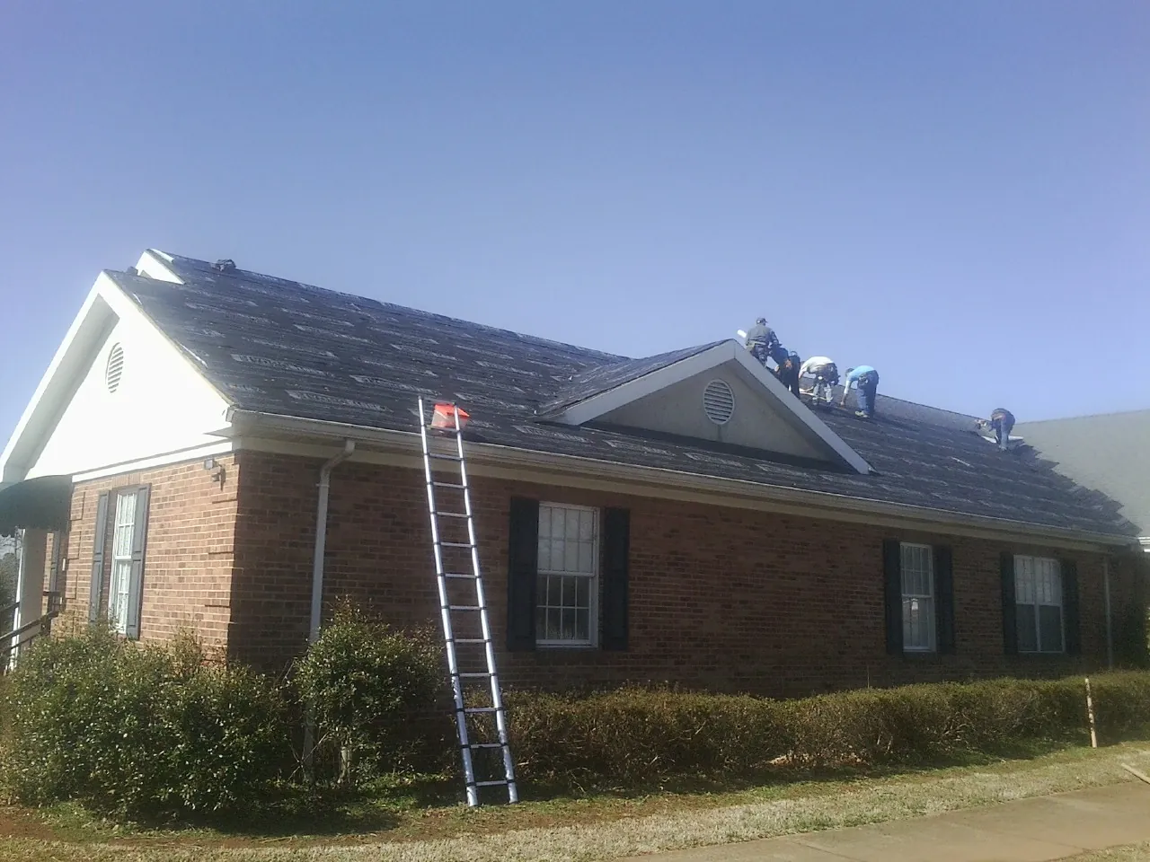 Crew tearing shingles off a brick ranch roof with a ladder set — Metal Roof Repair work by our crew in Portage
