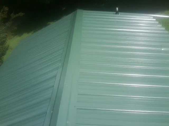 New green metal panels meeting at the ridge of a roof — Flat Roof Repair work by our crew in Portage