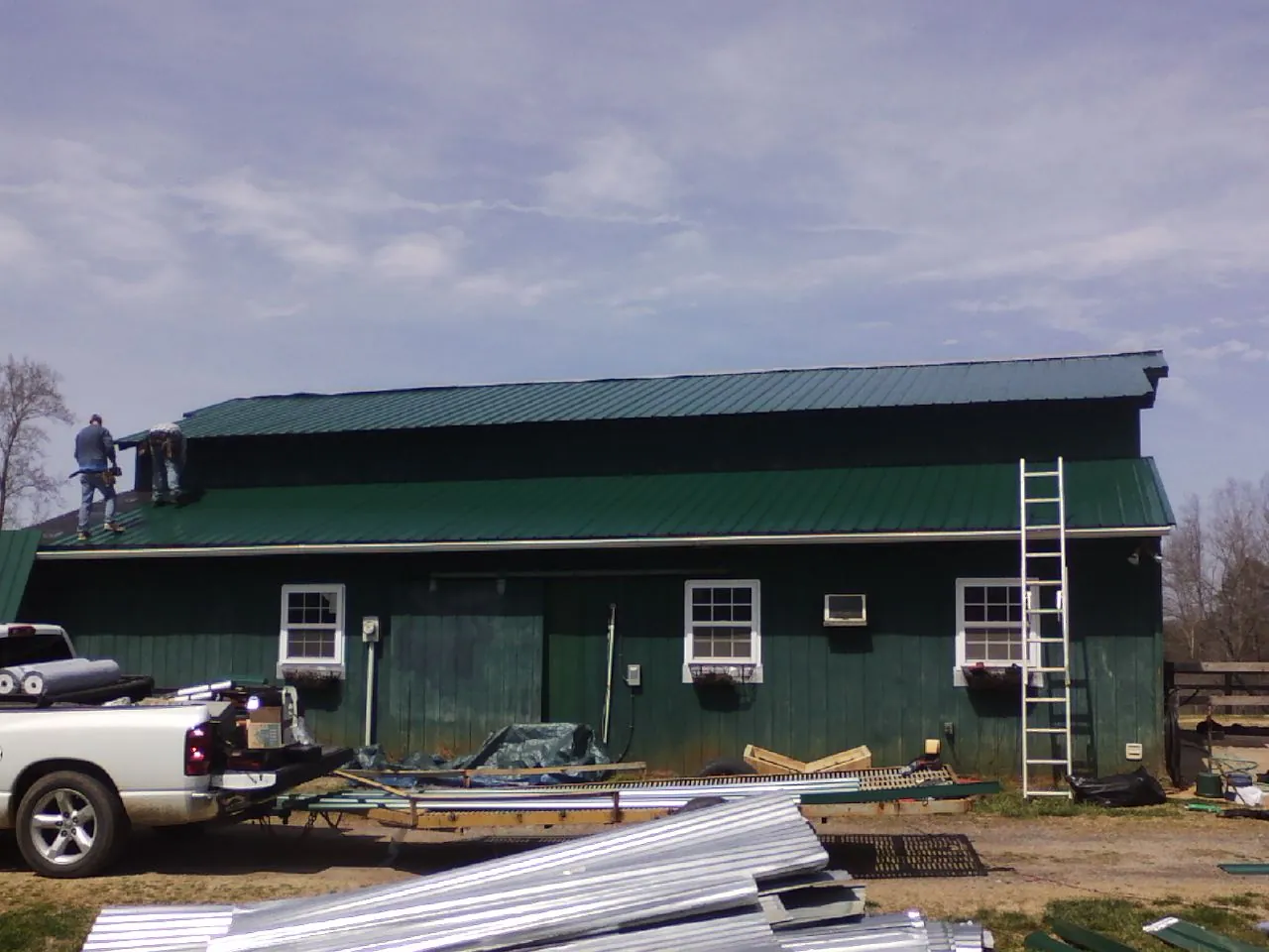 Crew installing green metal roofing on a large green barn in Portage