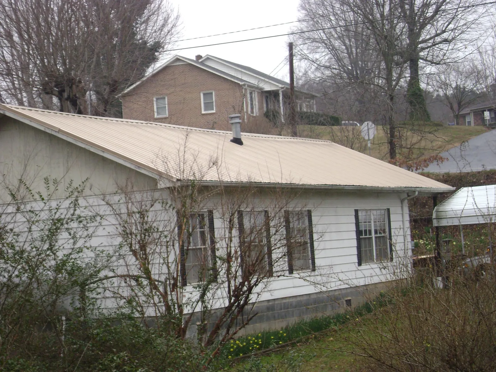 Tan metal roof on a white sided house set into a hillside — Commercial Roofing by Roofing Brothers in Portage